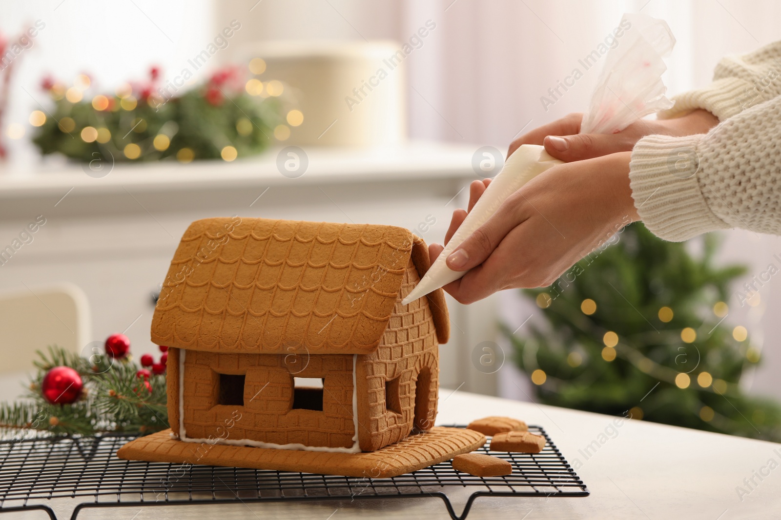 Photo of Woman making gingerbread house at white table, closeup