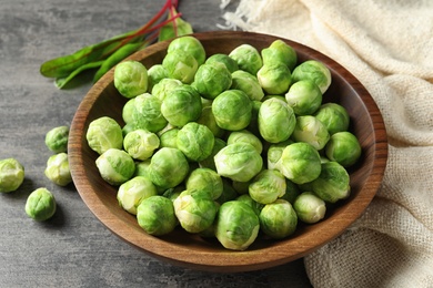 Photo of Bowl of fresh Brussels sprouts and napkin on grey table