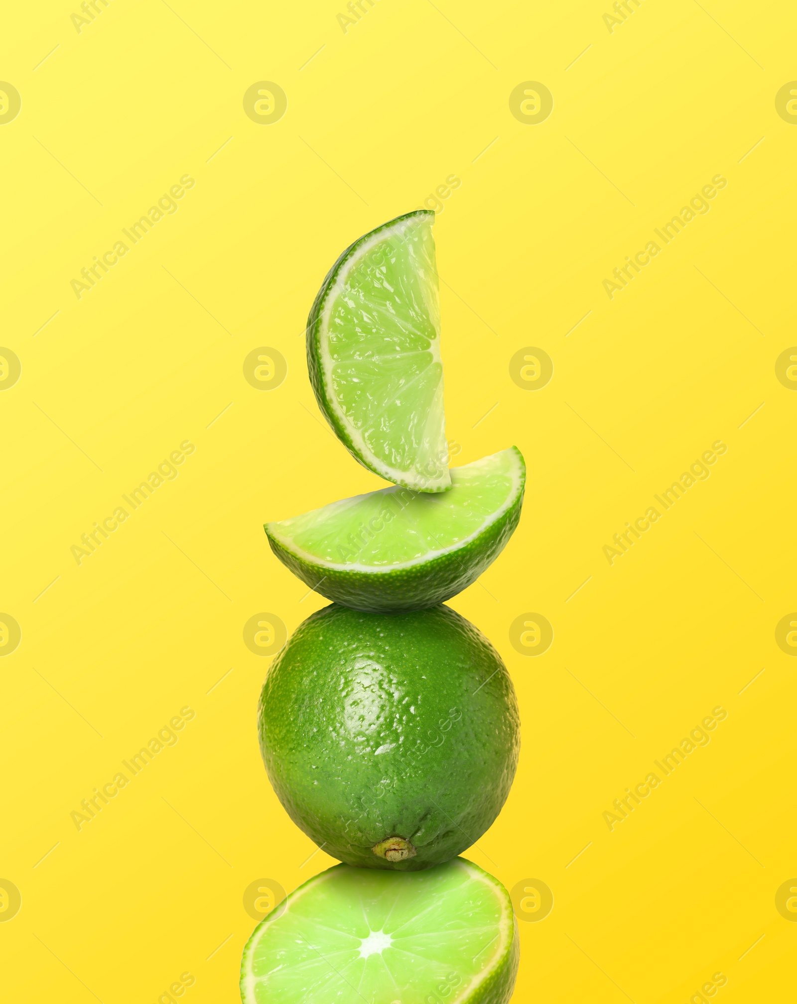 Image of Stacked whole and cut limes on yellow background