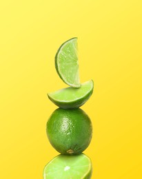 Image of Stacked whole and cut limes on yellow background