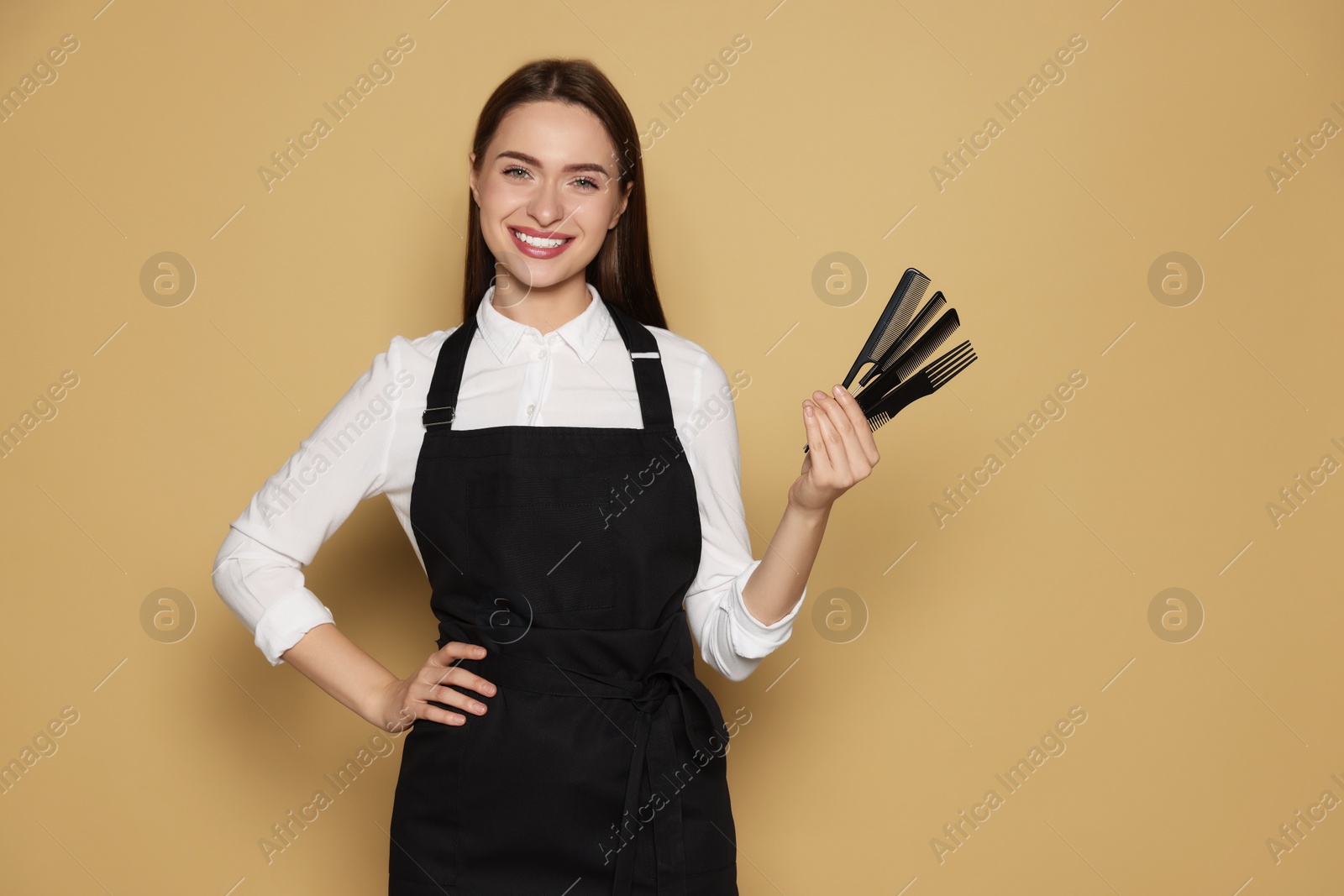 Photo of Portrait of happy hairdresser with combs on beige background. Space for text