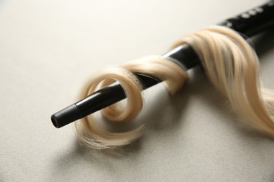 Modern clipless curling iron and blonde hair lock on grey background, closeup