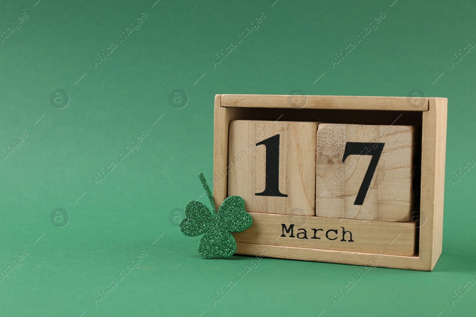 Photo of St. Patrick's day - 17th of March. Block calendar and decorative clover leaf on green background. Space for text