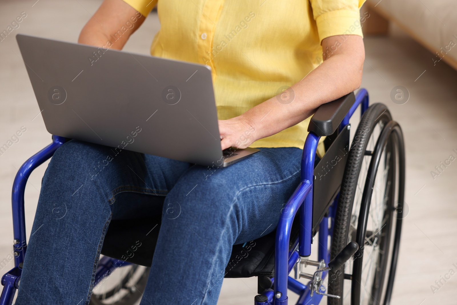 Photo of Woman in wheelchair using laptop indoors, closeup