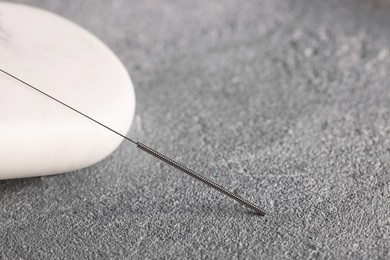 Photo of Acupuncture needle and spa stone on grey table, closeup. Space for text