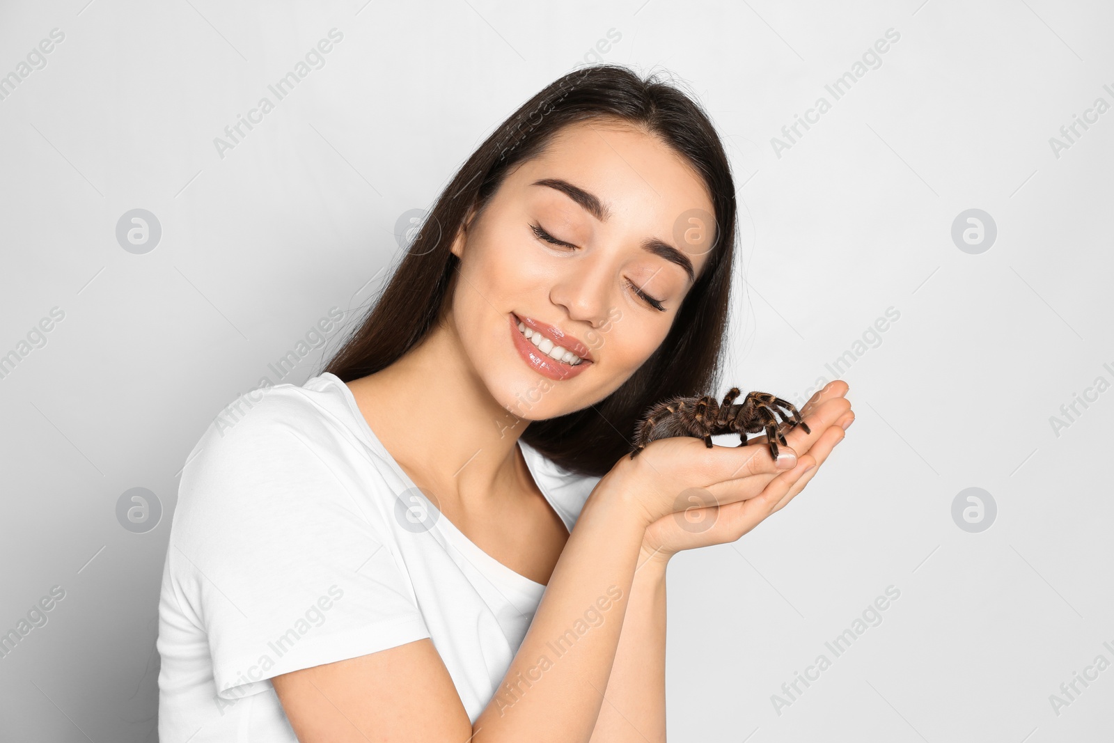 Photo of Woman holding striped knee tarantula on light background. Exotic pet