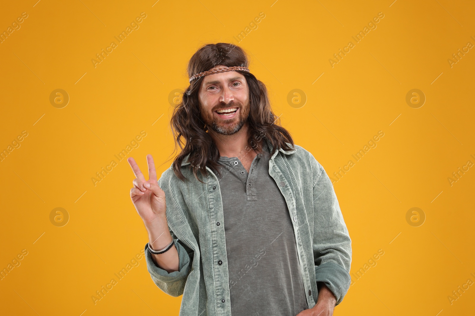 Photo of Stylish hippie man showing V-sign on orange background