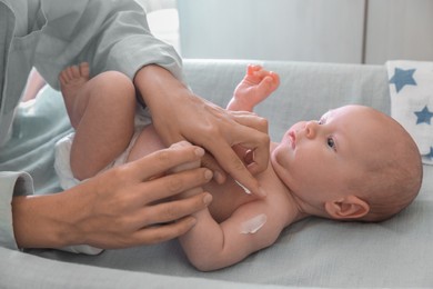 Photo of Mother applying moisturizing cream onto baby`s arm on changing table indoors, closeup