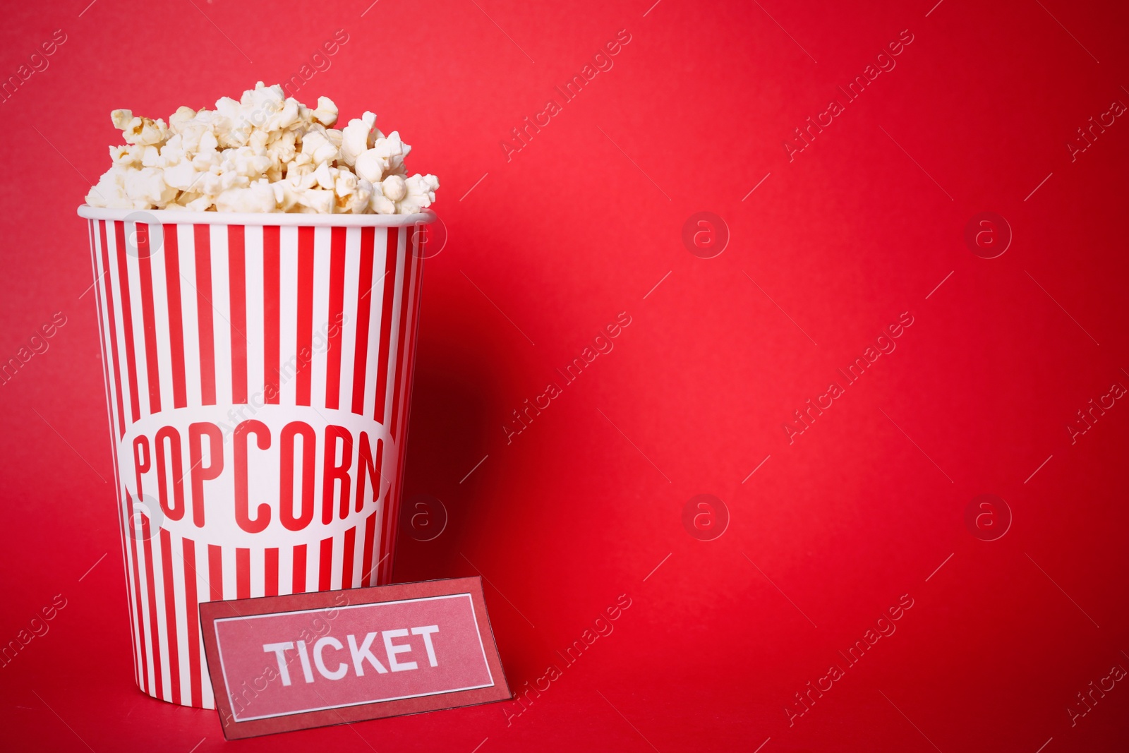 Photo of Delicious popcorn and ticket on red background. Space for text
