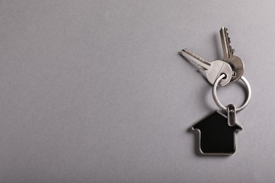 Photo of Keys with trinket in shape of house on grey background, top view and space for text. Real estate agent services