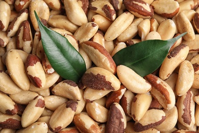 Photo of Many delicious Brazil nuts with green leaves as background, top view