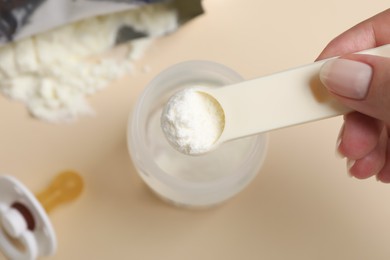 Photo of Woman preparing infant formula on beige background, top view. Baby milk