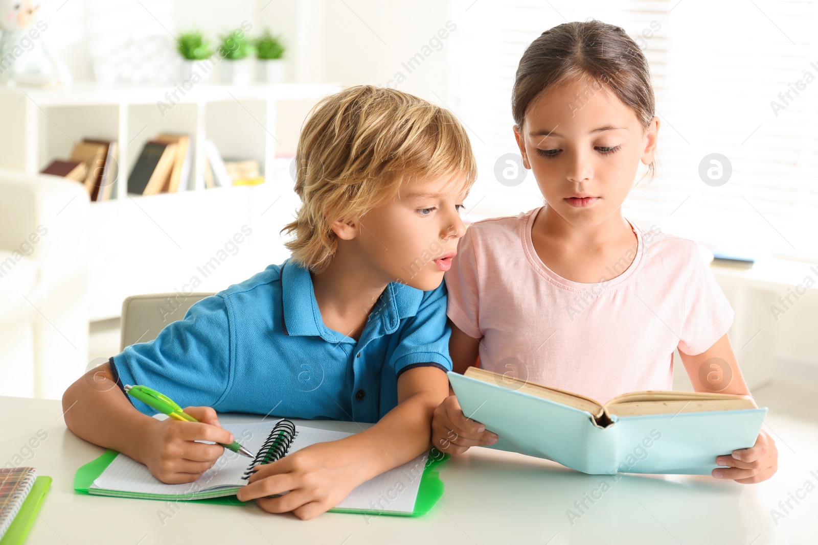 Photo of Little boy and girl doing homework at table indoors