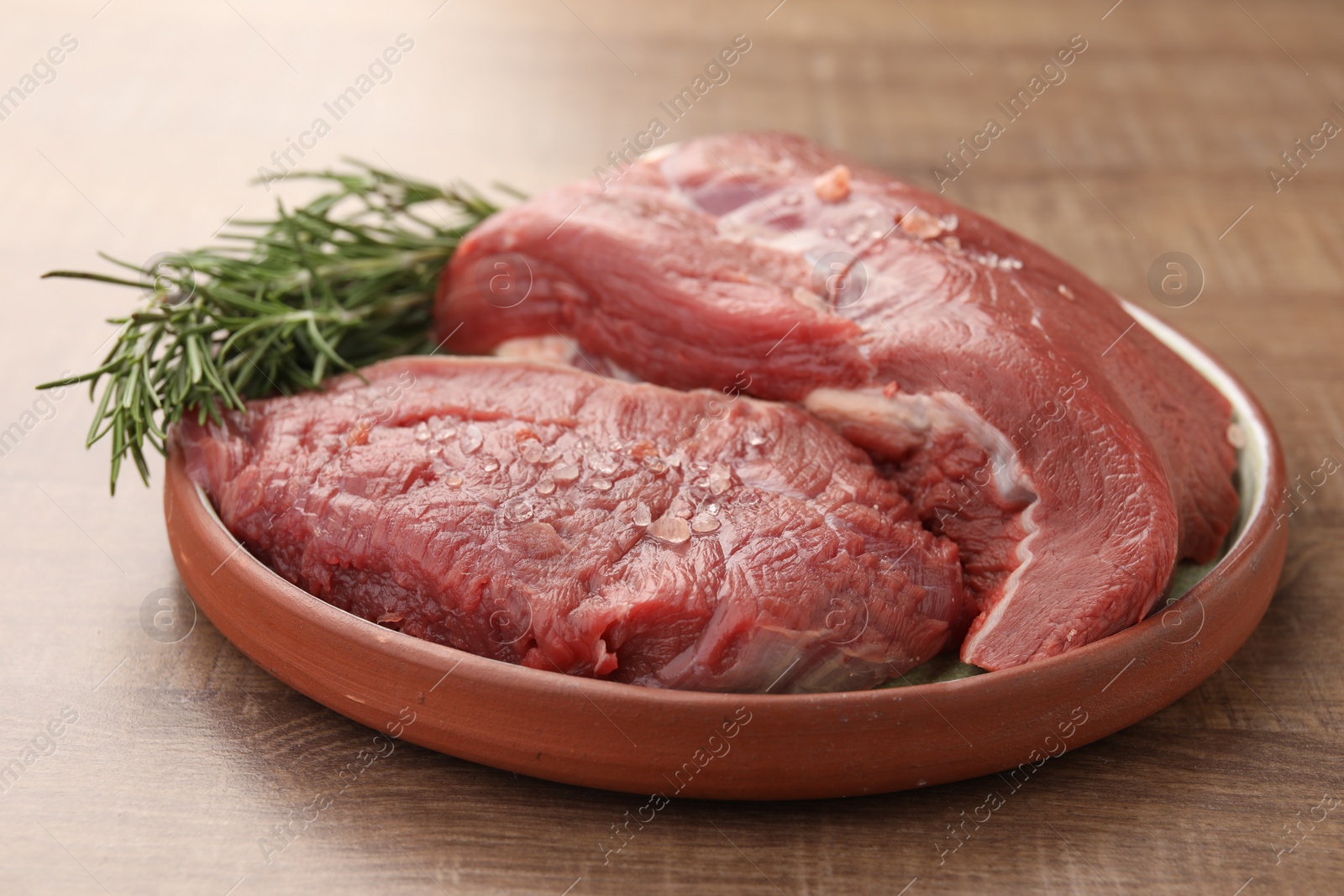 Photo of Pieces of raw beef meat with spices and rosemary on wooden table, closeup