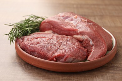 Pieces of raw beef meat with spices and rosemary on wooden table, closeup