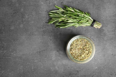 Photo of Jar of dried rosemary and fresh bunch on grey table, flat lay. Space for text