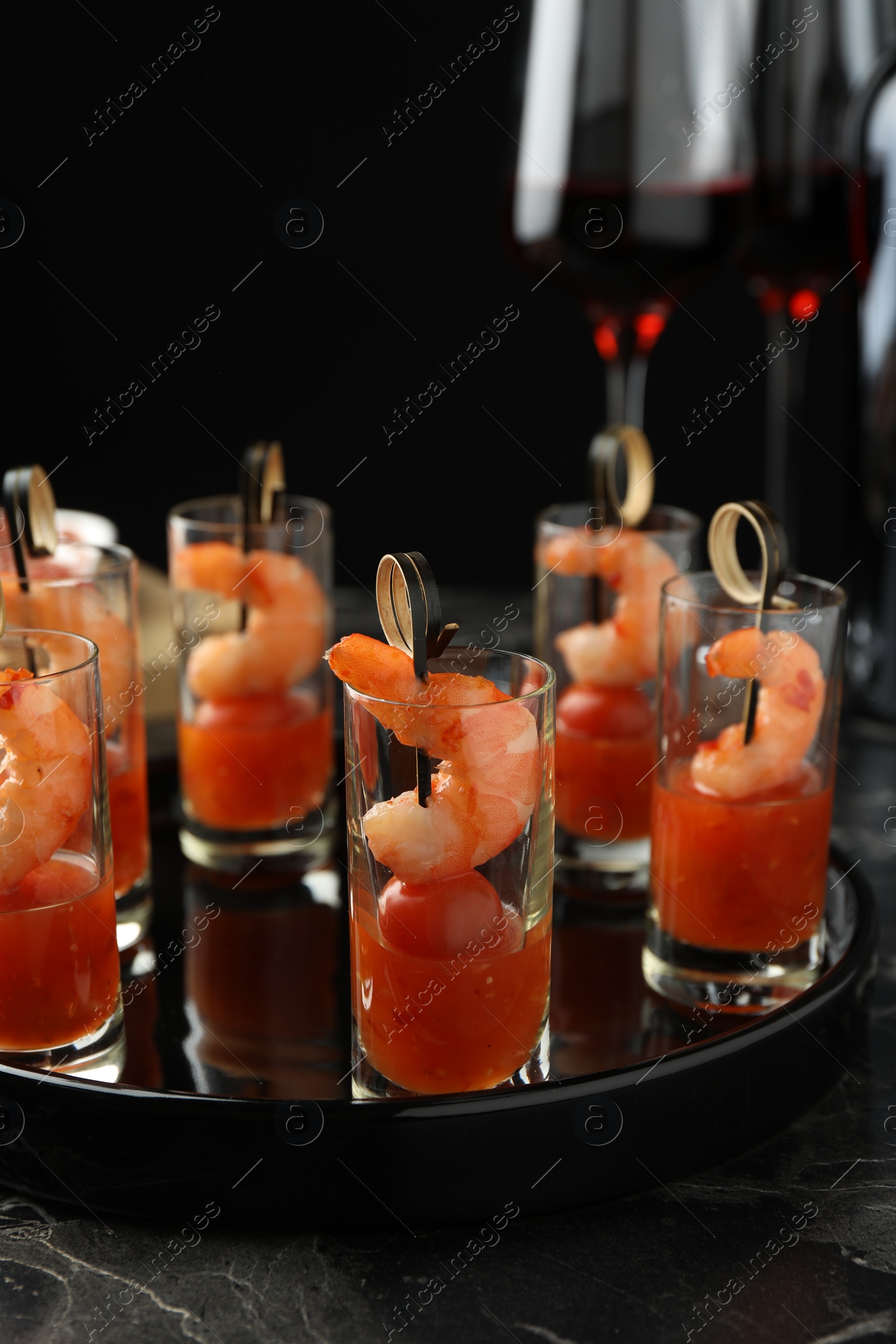 Photo of Tasty canapes with shrimps, tomatoes and sauce in shot glasses on black marble table, closeup