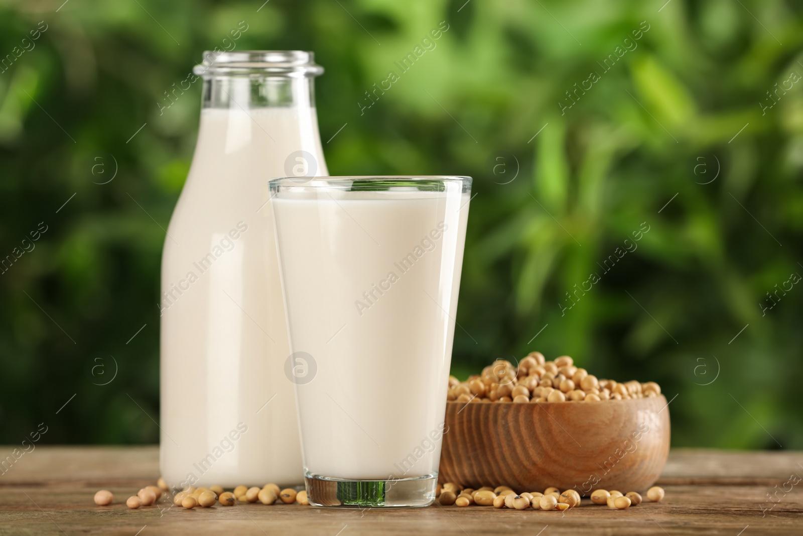 Photo of Fresh soy milk and grains on white wooden table against blurred background