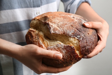 Photo of Woman breaking freshly baked bread on grey background, closeup