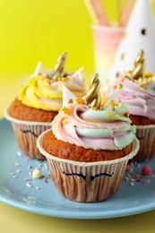 Photo of Cute sweet unicorn cupcakes and party items on yellow background, closeup