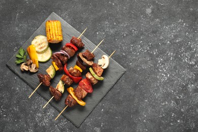 Photo of Delicious shish kebabs with grilled vegetables on grey textured table, top view. Space for text