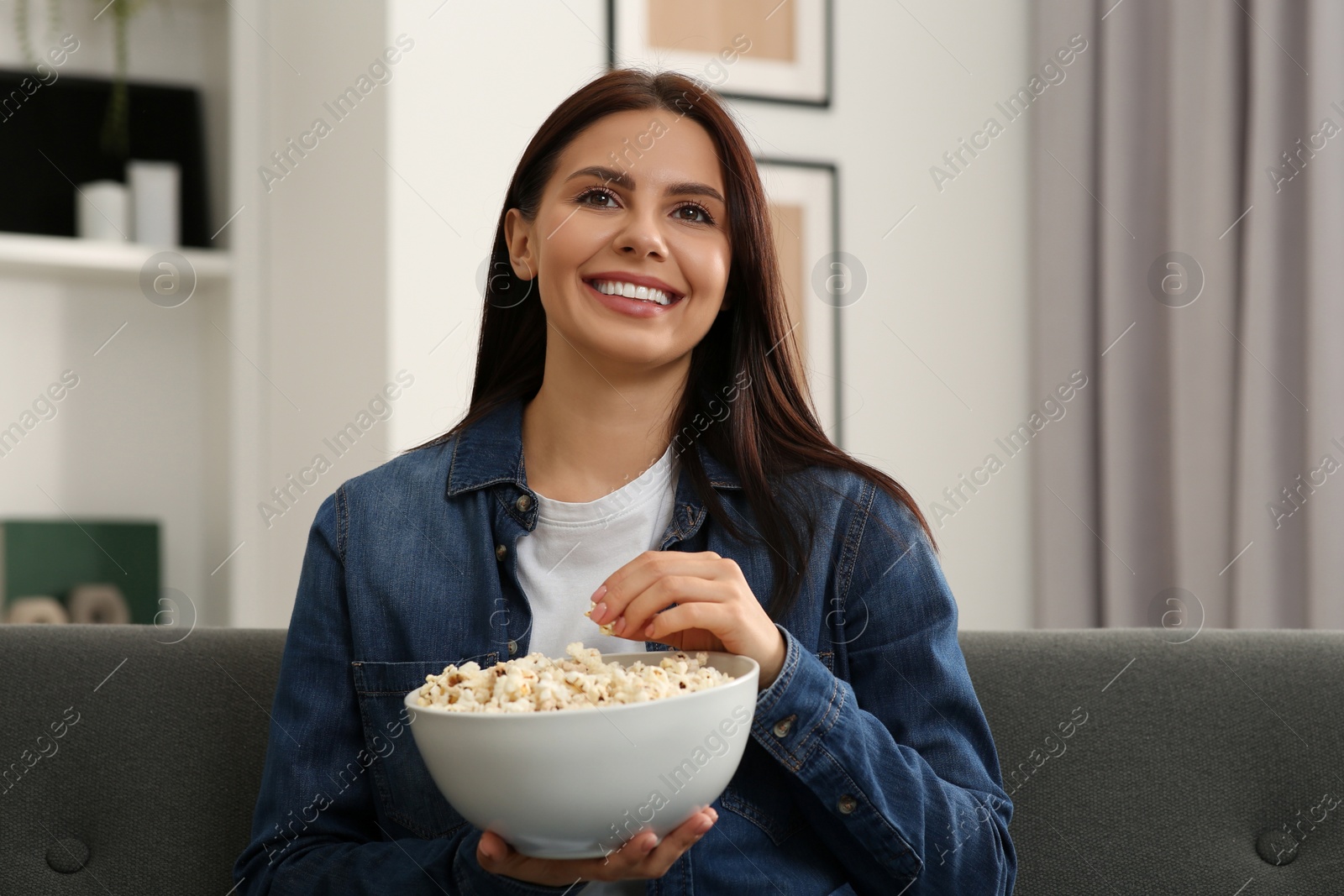 Photo of Happy woman with bowl of popcorn watching TV at home