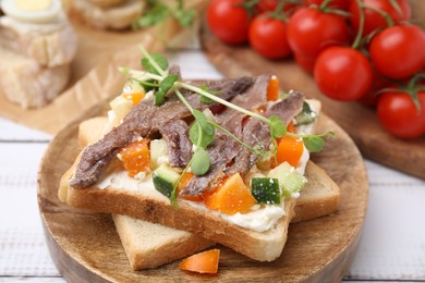Photo of Delicious toasts with anchovies, cream cheese, bell peppers and cucumbers on white wooden table, closeup