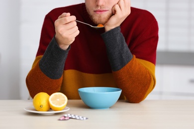 Sick young man eating soup to cure flu at table in kitchen