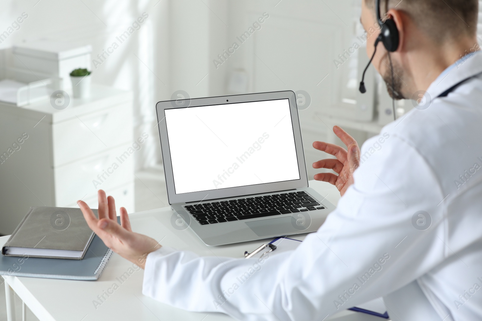 Photo of Doctor with headset consulting patient online at desk in clinic, space for text. Health service hotline