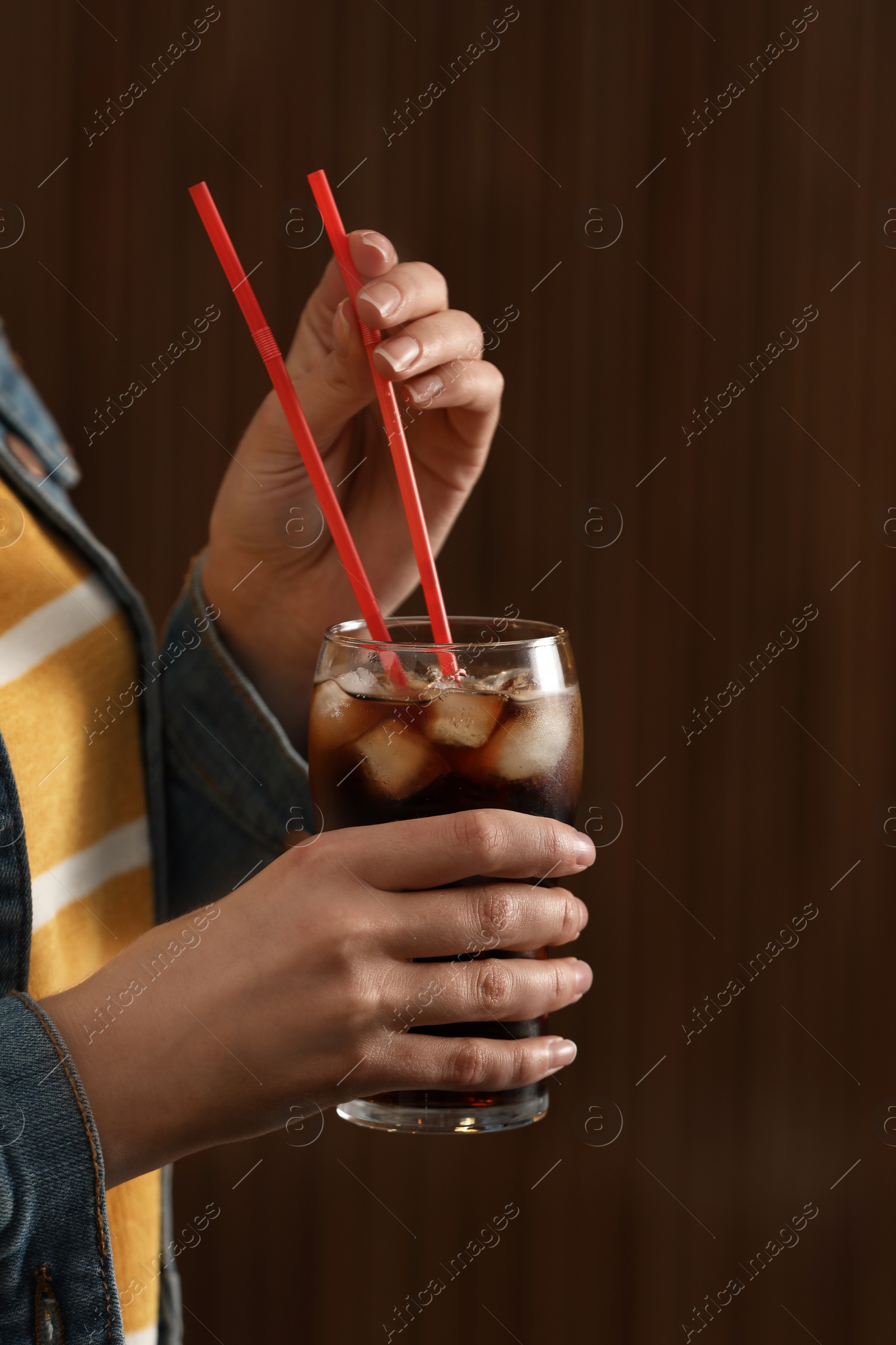 Photo of Woman holding glass of cola with ice against blurred background, closeup