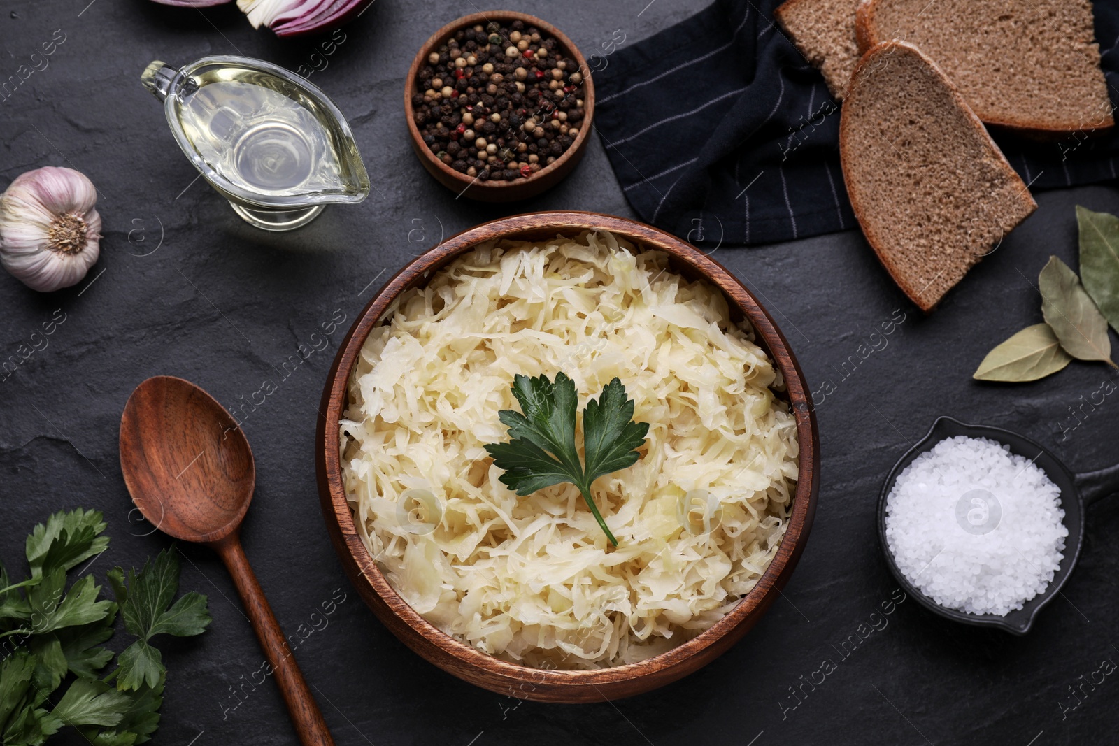 Photo of Bowl of tasty sauerkraut and ingredients on black table, flat lay