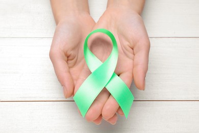 Photo of World Mental Health Day. Woman holding green ribbon on white wooden background, top view