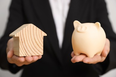 Woman holding piggy bank and house model on white background, closeup