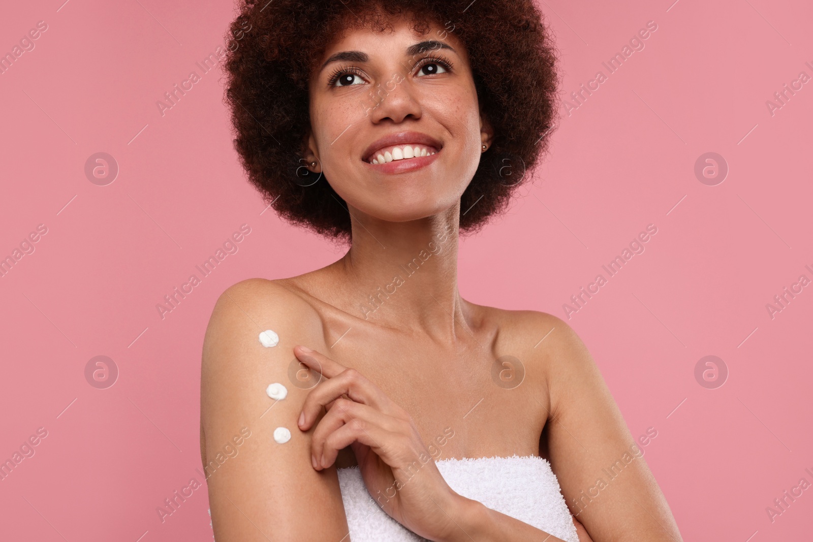 Photo of Beautiful young woman applying body cream onto arm on pink background