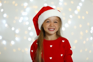 Photo of Happy little child in Santa hat against blurred festive lights. Christmas celebration