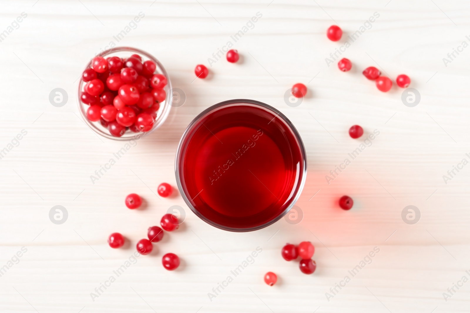 Photo of Tasty cranberry juice in glass and fresh berries on white wooden table, flat lay