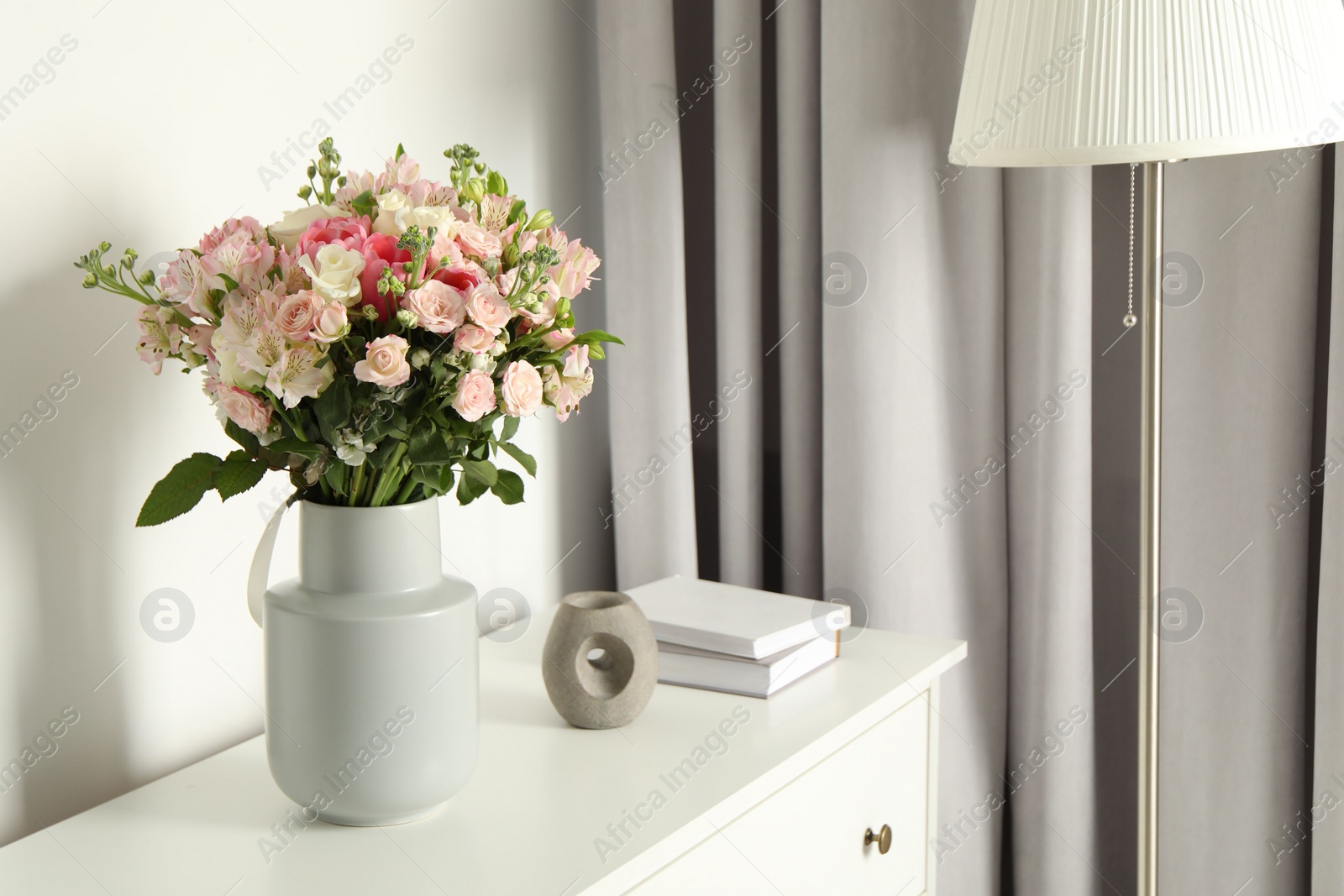 Photo of Beautiful bouquet of fresh flowers in vase on chest of drawers indoors