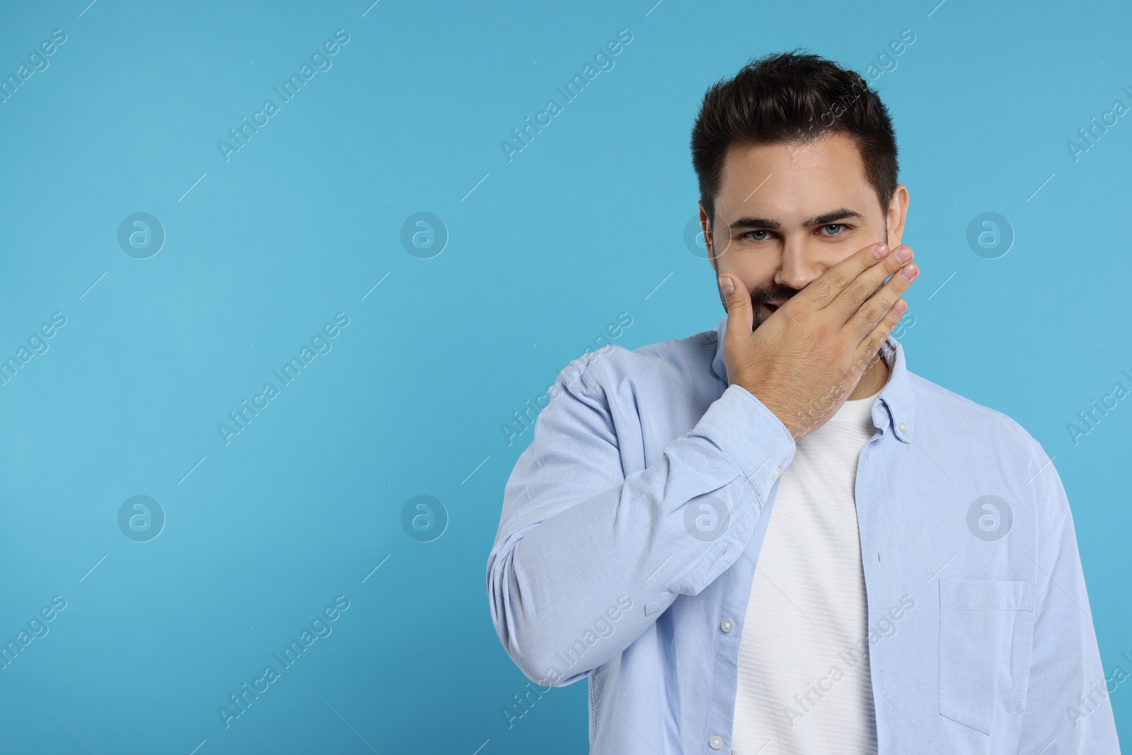 Photo of Embarrassed man covering mouth on light blue background. Space for text