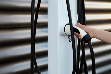 Photo of Woman taking plug from electric car charging station, closeup. Space for text