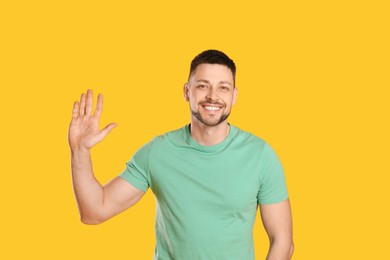 Photo of Cheerful man waving to say hello on yellow background