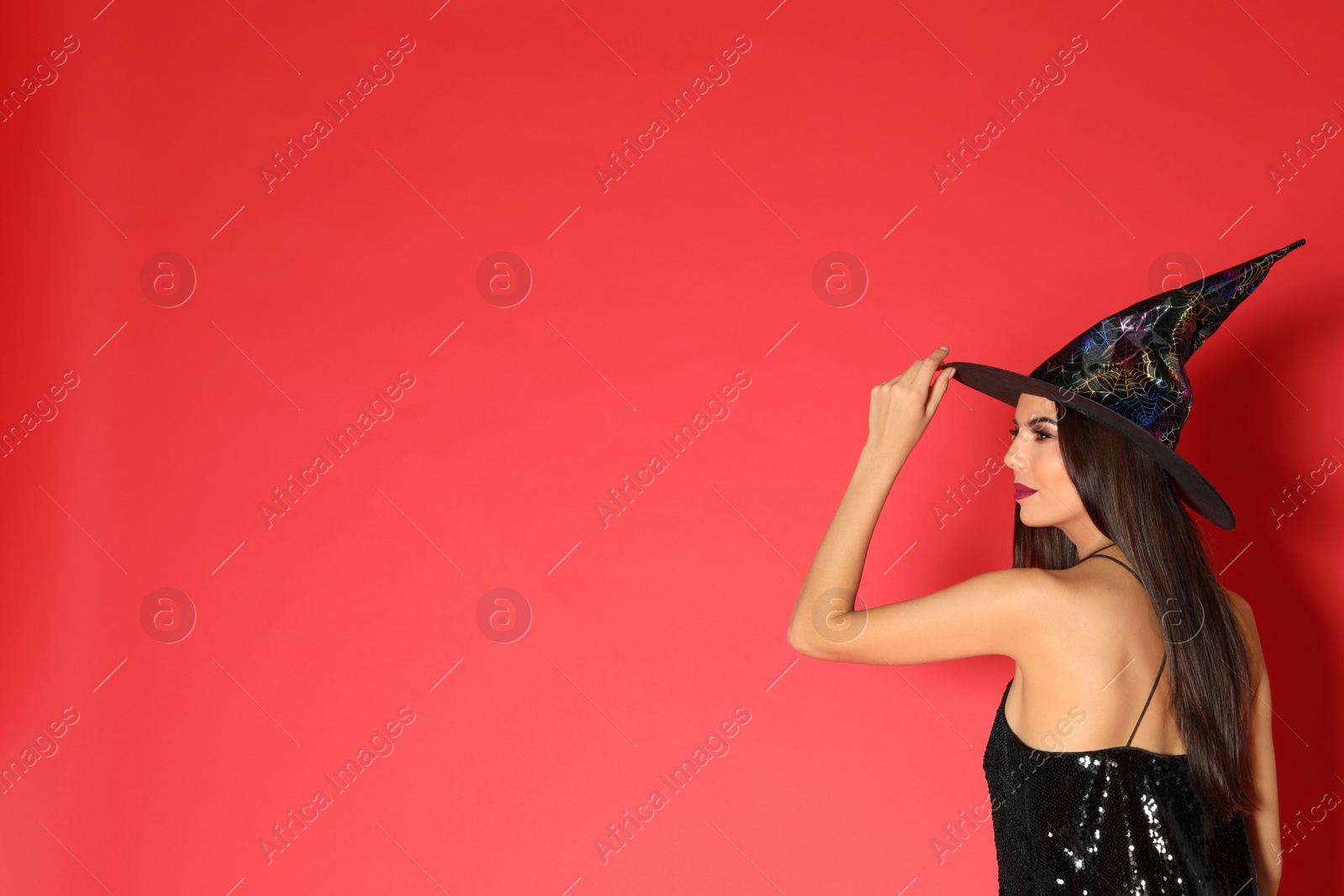 Photo of Beautiful young woman wearing witch costume for Halloween party on red background, space for text