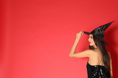 Beautiful young woman wearing witch costume for Halloween party on red background, space for text