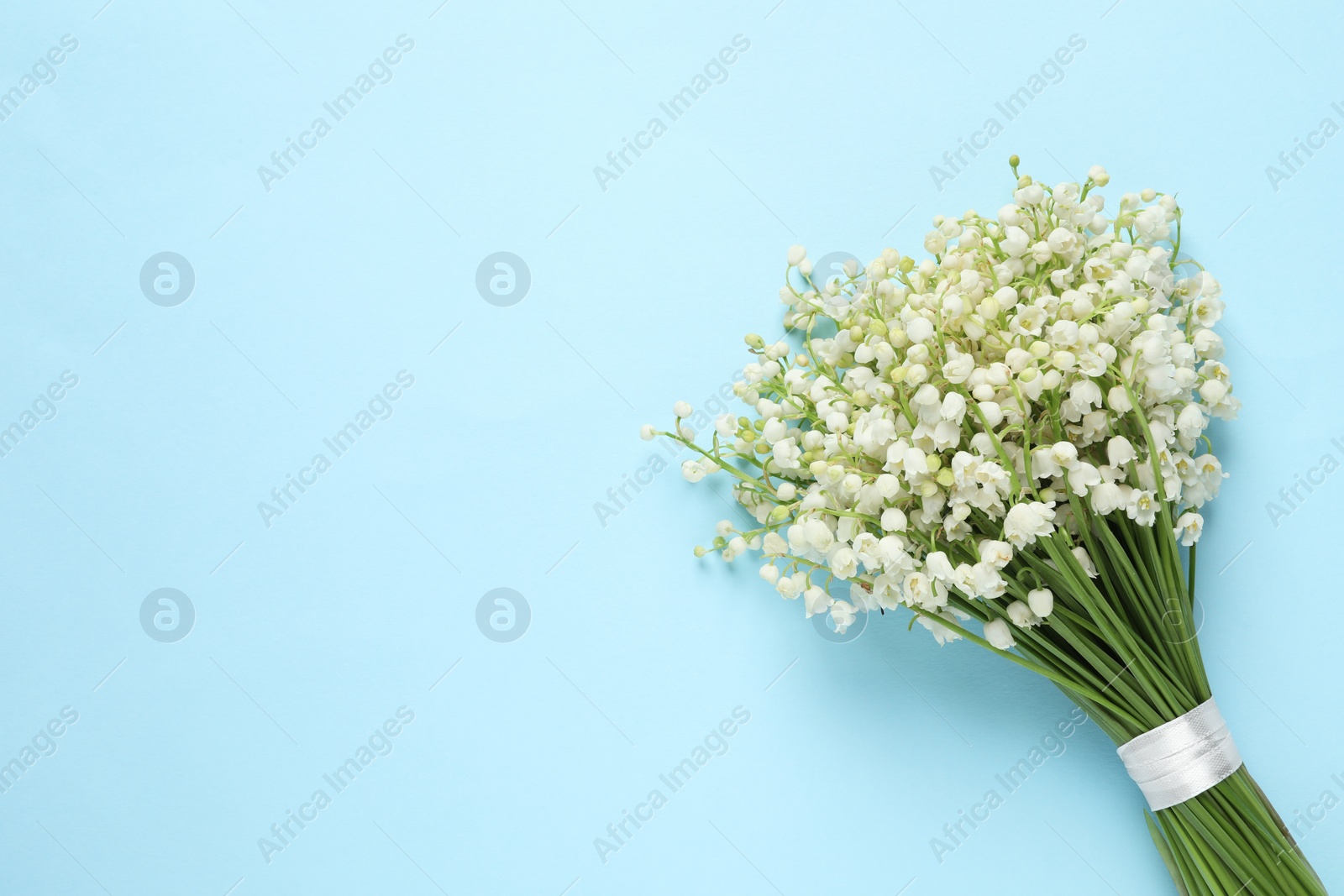 Photo of Beautiful lily of the valley bouquet on light blue background, top view. Space for text