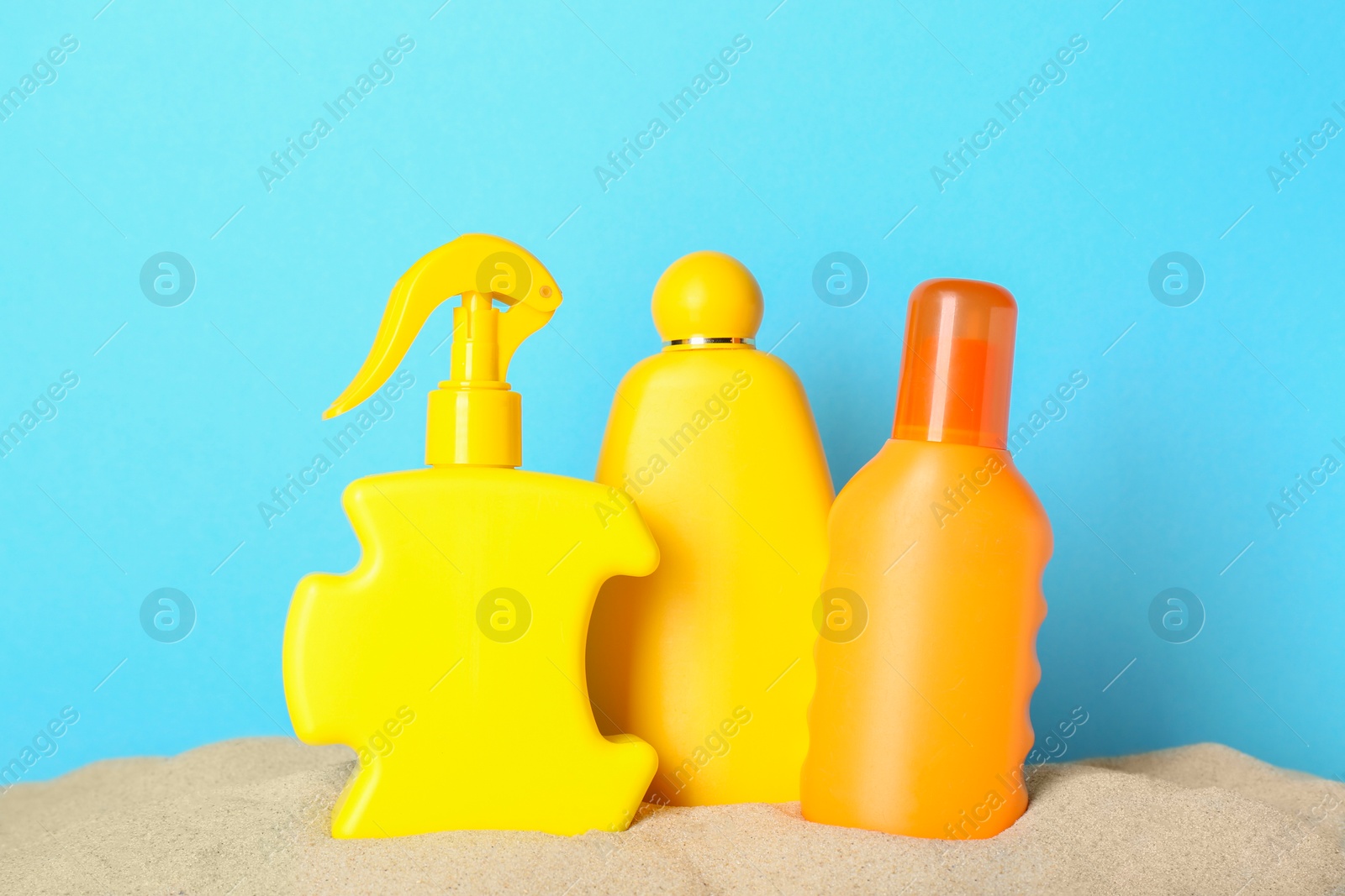 Photo of Many different suntan products in sand against light blue background