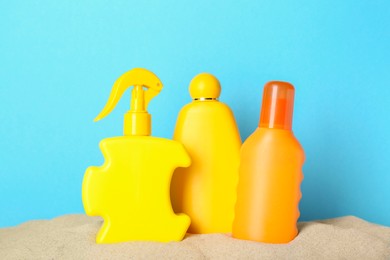 Photo of Many different suntan products in sand against light blue background