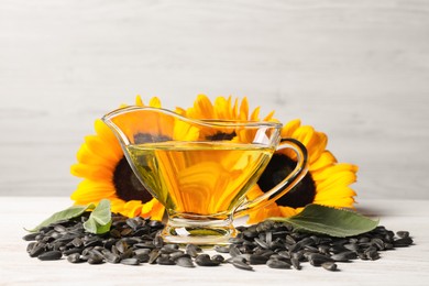 Sunflower cooking oil, seeds and yellow flowers on white wooden table