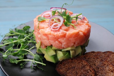 Tasty salmon tartare with avocado, microgreens and croutons on table, closeup