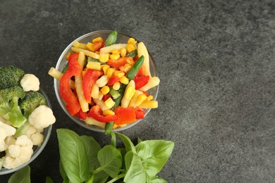 Bowls of different frozen vegetables and fresh basil on grey table, flat lay. Space for text