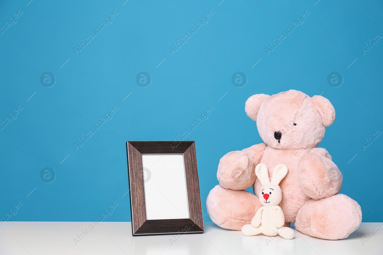 Photo of Photo frame and adorable toys on table against color background, space for text. Child room elements