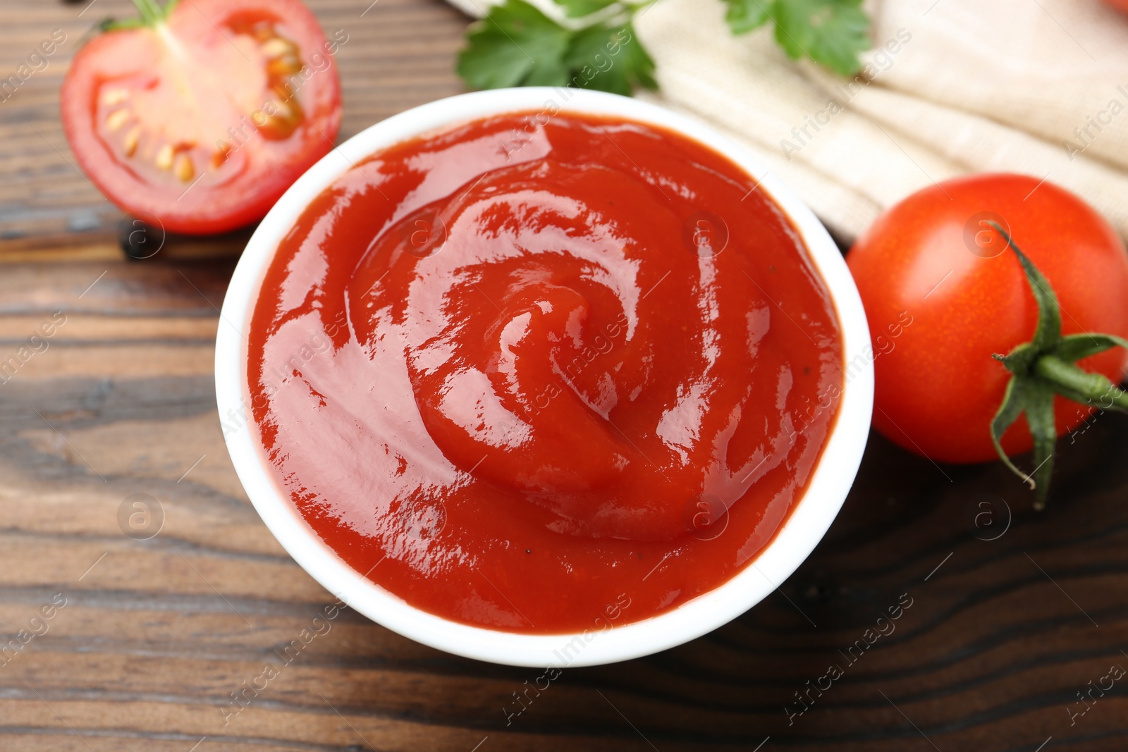 Photo of Delicious ketchup in bowl and tomatoes on wooden table, closeup